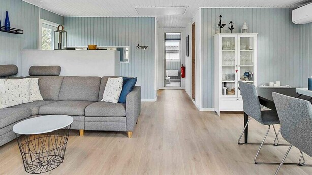 Ein modernes Wohnzimmer mit grauem Sofa, einem runden Couchtisch und einem Essbereich mit weißem Schrank und grauen Stühlen.