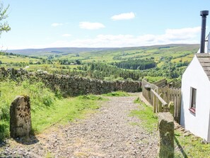 A rural landscape with a stone wall, a gravel path, and a white building with a chimney. - Dale View Cottage: Cozy Retreat (Hexham)