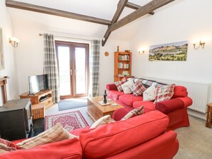 A living room with a red sofa, a wooden bookshelf, a television, and a painting on the wall. - Dale View Cottage: Cozy Retreat (Hexham)
