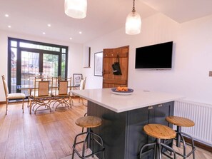 Une cuisine moderne dotée d’un grand îlot central, de tabourets de bar, d’un coin repas avec des chaises et d’un téléviseur fixé au mur.