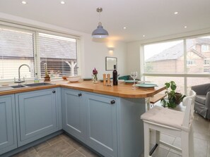 A kitchen with a blue cabinet, a wooden countertop, a pendant light, and a dining area with a white chair. - Kestrel, Tilston: A Charming Retreat (Malpas)