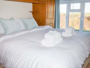 A neatly made bed with white linens, a wooden headboard, and a window with a view of the outdoors. - Smugglers' Cottage, Marske-By-The-Sea (Redcar)
