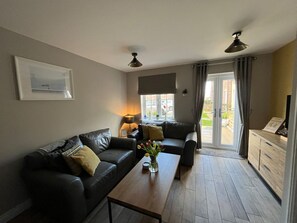Ein Wohnzimmer mit einer Couch, einem Couchtisch mit Blumen, einer Lampe und Blick ins Freie.