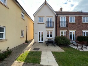 Ein Wohngebäude mit gepflasterter Terrasse, Sitzgelegenheiten im Freien und einem kleinen Garten.
