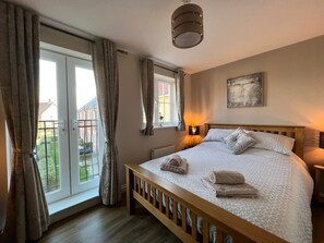 Ein Schlafzimmer mit einem Bett, Vorhängen, einem Fenster, einer Wandlampe und einem Gemälde.