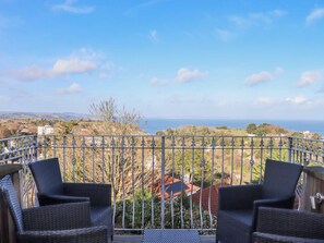 A balcony with wicker chairs, a metal railing, and a view of the sea and distant landscape. - Flat 3 Channel View, Torquay (Torquay)