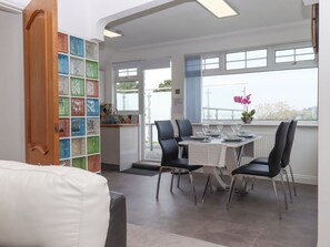 A dining area with a table set for four, black chairs, and a view of the outdoors through large windows. - Flat 3 Channel View, Torquay (Torquay)