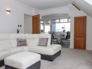 A modern living room with a sectional sofa, a dining area with a table and chairs, and a large window with a view. - Flat 3 Channel View, Torquay (Torquay)