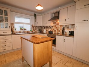 A kitchen with white cabinets, a wooden island, a window, and a tiled backsplash.