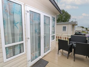 A covered patio with a sliding glass door, a small outdoor seating area with wicker furniture, and a white fence in the background. - 50, Foxburrow Hang, in Norfolk (Great Yarmouth)