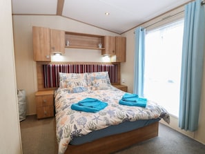 A bedroom with a bed, nightstands, a wooden headboard, built-in shelves, and a large window with curtains. - 50, Foxburrow Hang, in Norfolk (Great Yarmouth)