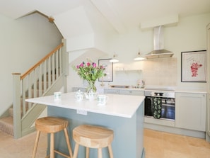 A kitchen with a white island, wooden stools, a stainless steel oven, and a staircase. - Charming Oak Home in Elcot (Newbury)