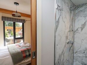 A bedroom with a bed, a window, and a shower with marble walls.