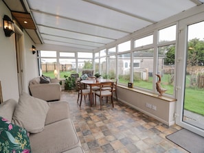 A conservatory with a checkered floor, a sofa, a table with chairs, and a view of the outside. - Kouloura, Southerness (Dumfries)