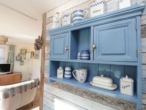 Un buffet en bois bleu contenant de l’ustensile de cuisine, une télévision et un canapé à motifs.