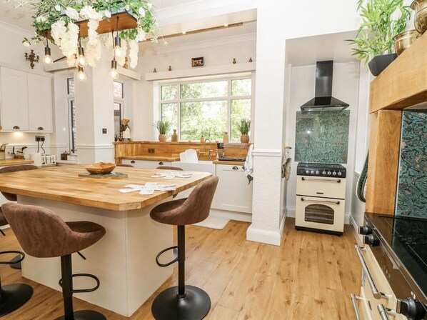 A kitchen with a wooden island, bar stools, a stove, and a window with plants. - Bentfield House, Whiston (Rotherham)