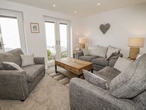 Ein Wohnzimmer mit zwei Sofas, einem Couchtisch und zwei Lampen. Zwei Türen führen zu einem Balkon.