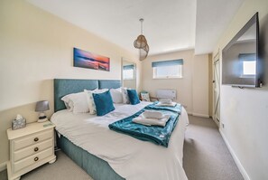 Ein Hotelzimmer mit Bett, Nachttisch, Lampe, Kunstwerk und Fernseher.