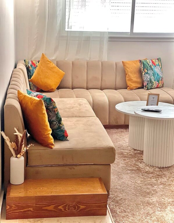 A modern living room with a beige sofa, colorful pillows, a white coffee table, and a wooden side table.