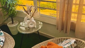 Un balcón con vista a un edificio, una planta en maceta, un jarrón decorativo y mobiliario de mimbre.