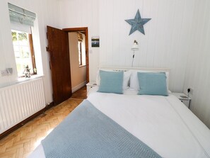 A bedroom with a bed, a star decoration, a nightstand, a lamp, a window, and a door. - Fox Cottage, Droitwich Spa (Droitwich)