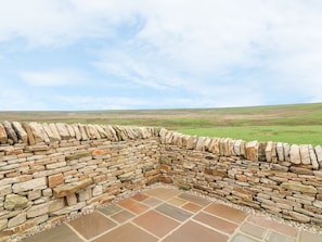 Espacio al aire libre con paredes de piedra y vistas a un paisaje con césped.