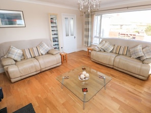 A living room with two beige sofas, a glass coffee table, and a door with a shoe rack. - Meadow View, Letterston (Haverfordwest)