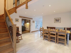 A spacious room with a wooden staircase, a dining area with wooden chairs and a table, and a hallway leading to another room. - Y Stabl, Cerrigydrudion (Corwen)