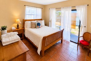 A hotel room with a wooden bed, a bedside table with a lamp, a chair with a red cushion, and a view of the outside. - Spacious 4 bedroom Home in Sarasota Sleeps 11 Near Beaches, Airport & Dining (Sarasota)