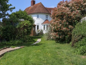 A white house with a red roof, surrounded by greenery and a garden path. - HOP HOUSE: Cozy Retreat with WiFi (Hastings)