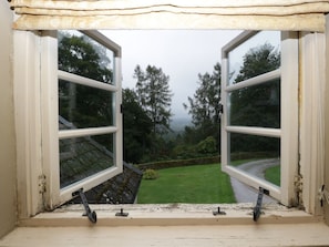 Ein offenes Fenster mit Blick auf eine grüne Wiese und Bäume.