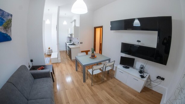 Un espacio habitable compacto con kitchenette, comedor y zona de estar con sofá y sillones.