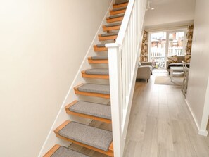 Eine Treppe mit Holzdielen und grauen Teppichböden führt zu einem Wohnbereich mit Sofa und Tisch.