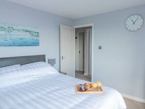 A bedroom with a bed, a painting, a clock, and a breakfast tray.