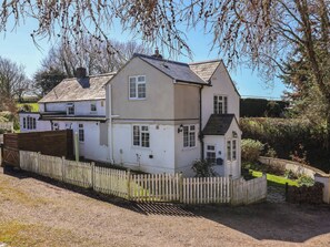 A two-story house with a white exterior, a wooden fence, and a small garden area. - The Old Smithy, Dottery (Bridport)
