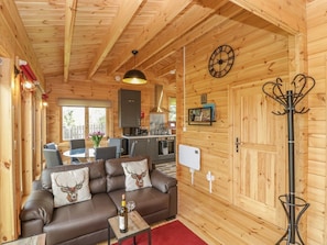 Interno di una baita in legno con divano, tavolo da pranzo, angolo cottura e un orologio appeso al muro.