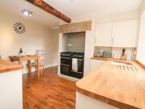 A kitchen with a wooden countertop, a stove, cabinets, and a dining area with a table and chairs. - Cottage Round T'Corner, Honley (Holmfirth)