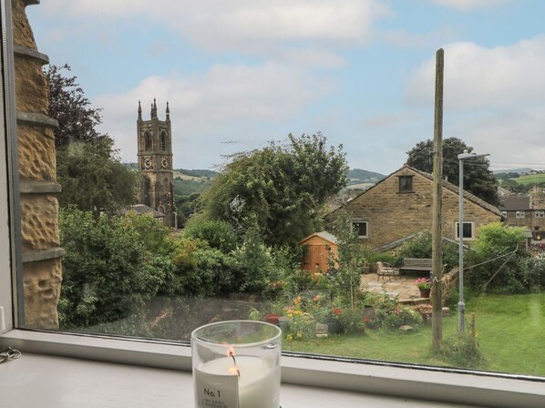 A window view of a rural landscape with a stone building, a wooden fence, and a distant church tower. - Cottage Round T'Corner, Honley (Holmfirth)