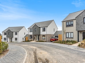 Une rue résidentielle bordée de maisons modernes, avec une voiture rouge et une allée pavée.