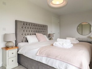 Une chambre à coucher bien rangée, avec une tête de lit capitonnée, une table de chevet avec une lampe, un miroir et des serviettes soigneusement pliées.