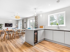 Une cuisine moderne avec des meubles blancs, un lave-vaisselle encastré et un coin repas comprenant des chaises et une table en bois.