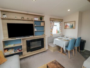 Ein Wohnzimmer mit Flachbildfernseher, Kamin, Esstisch mit Stühlen und einem fenster mit Vorhängen.