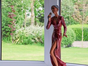 A statue of a person in a red dress standing by a window with a view of a garden. - The Annexe is in Burton Pidsea (Hull)