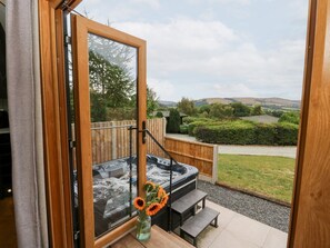 A hot tub outside a wooden door, a wooden bench, and a vase with flowers. - Dam View Shepherds Hut, Rhayader (Rhayader)