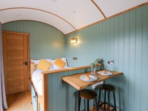 A room with a bed, a small wooden table with two stools, a wall-mounted light fixture, and a door. - Dam View Shepherds Hut, Rhayader (Rhayader)