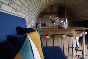 An interior with a brick wall, a wooden bar with stools, a sink, and a blue couch with cushions. - Badgers View, Rhayader, Wales. (Rhayader)