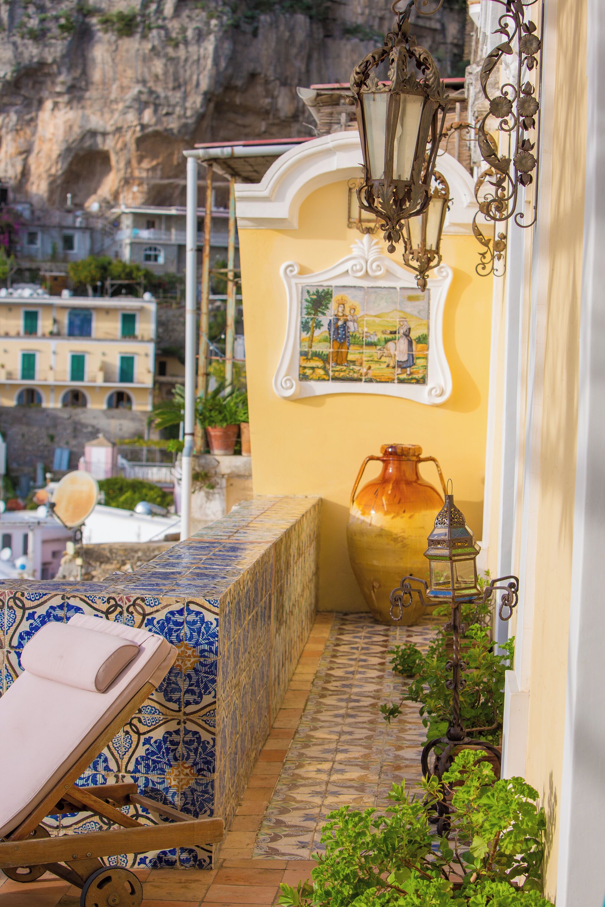 A balcony with a chair, a large vase, and a wall-mounted lamp.