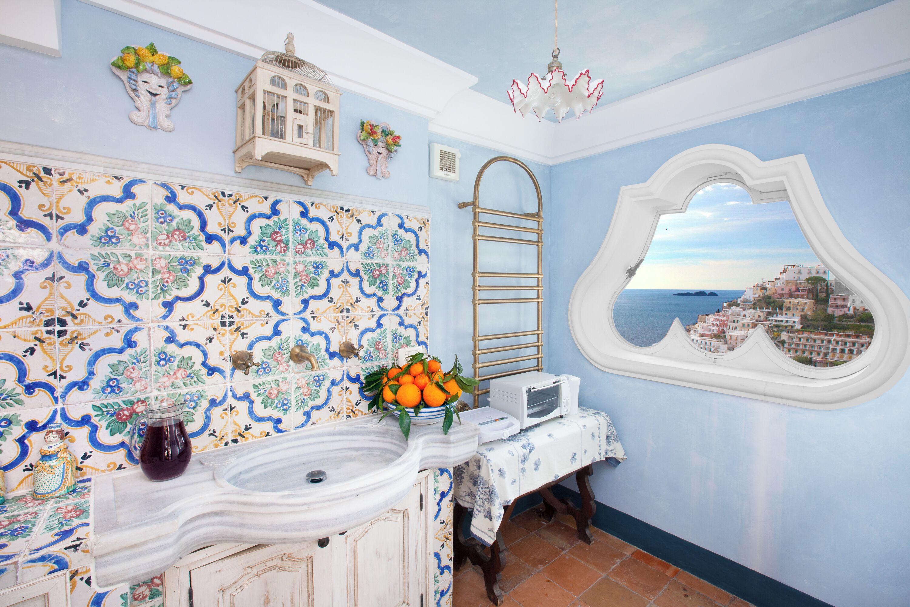 Een badkamer met een betegelde spatwand, een wastafel, een spiegel met uitzicht, een handdoekhouder en een decoratieve lantaarn.