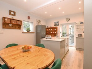 A modern kitchen with a central island, wooden dining table, and green chairs. - Primose Cottage, Cromer, Norfolk (Cromer)