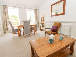 Ein Zimmer mit Holztisch, Stühlen, Heizkörper, einem Fenster mit Vorhängen und einem Spiegel an der Wand.